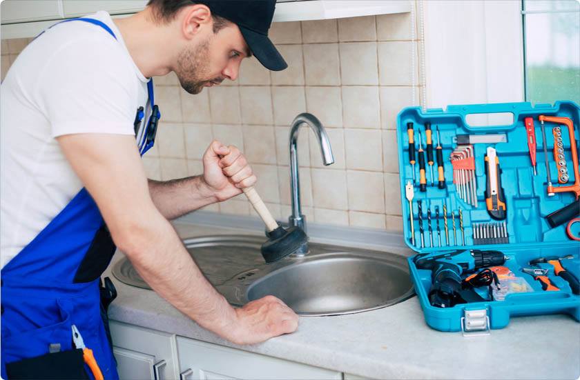 A plumber is trying to unclog a kitchen sink using tools.